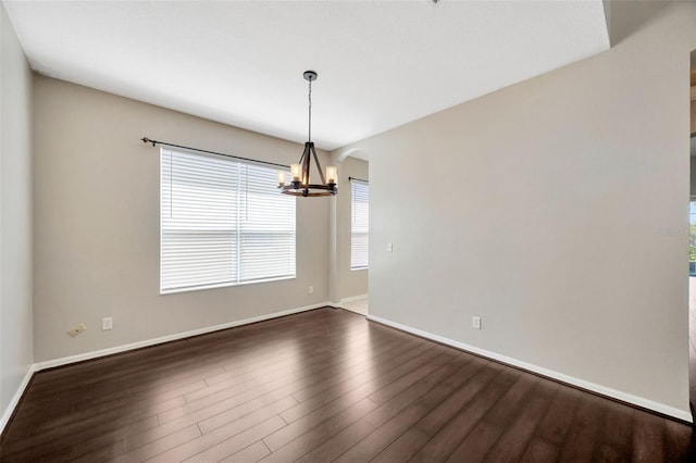 unfurnished room with dark wood-style floors, a notable chandelier, arched walkways, and baseboards