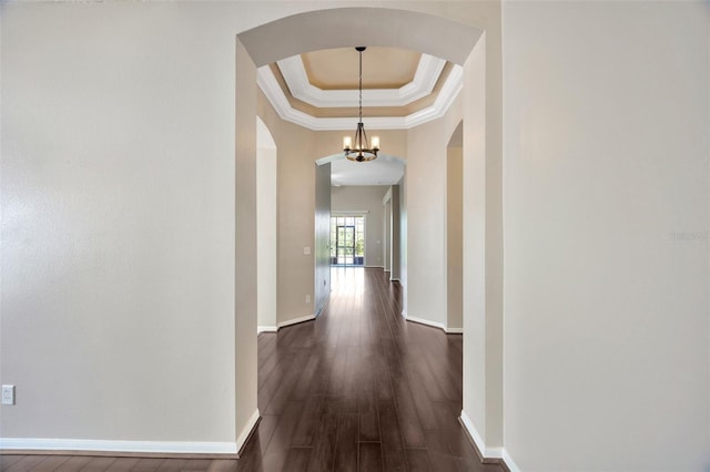 corridor featuring a tray ceiling, dark wood-style floors, arched walkways, crown molding, and baseboards