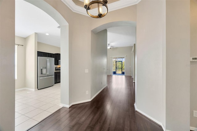 hall with baseboards, arched walkways, light wood finished floors, and a chandelier