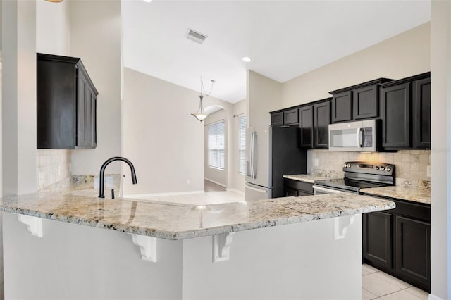 kitchen featuring visible vents, a breakfast bar, light tile patterned floors, a peninsula, and stainless steel appliances