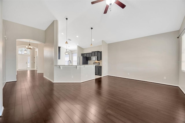 unfurnished living room featuring dark wood-type flooring, ceiling fan with notable chandelier, arched walkways, and a sink