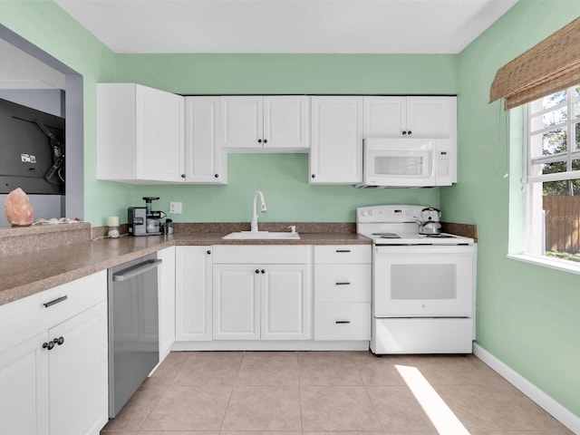 kitchen with a sink, white appliances, white cabinets, light tile patterned floors, and baseboards