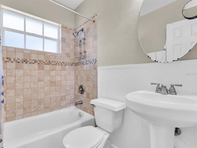 full bathroom featuring shower / bath combo, a sink, wainscoting, toilet, and a textured wall