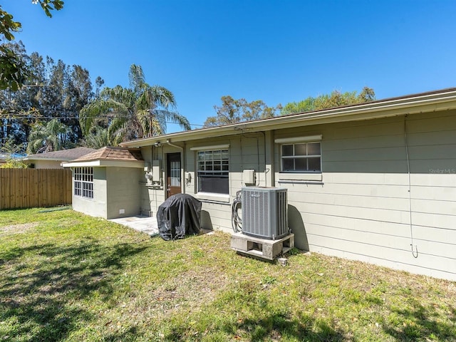 rear view of house featuring cooling unit, a yard, and fence