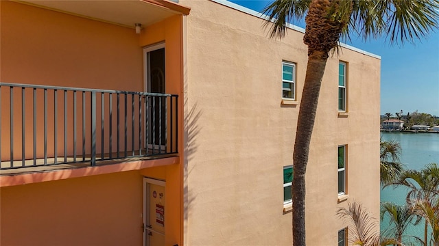 view of property exterior featuring stucco siding, a water view, and a balcony