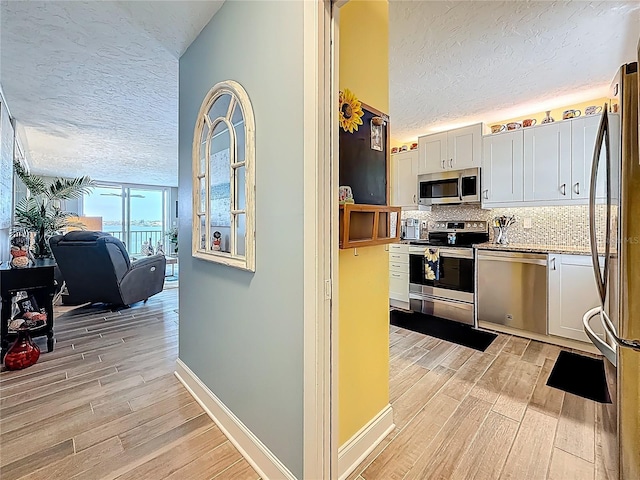 kitchen featuring tasteful backsplash, a textured ceiling, appliances with stainless steel finishes, white cabinets, and light wood finished floors