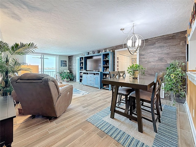 dining area featuring wood tiled floor, a notable chandelier, wood walls, and a textured ceiling