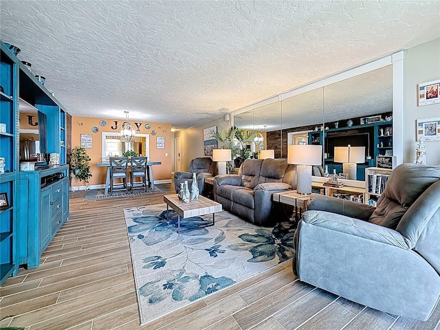 living room with a textured ceiling, an inviting chandelier, baseboards, and wood finish floors