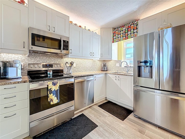 kitchen with light wood-type flooring, a sink, a textured ceiling, stainless steel appliances, and decorative backsplash