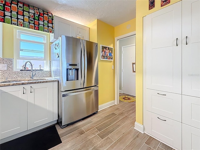 kitchen featuring decorative backsplash, wood finish floors, stainless steel fridge, and a sink