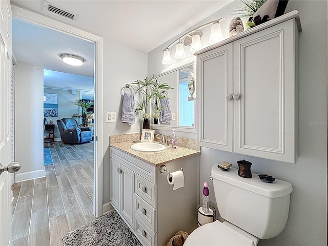 bathroom featuring vanity, baseboards, visible vents, wood finish floors, and toilet