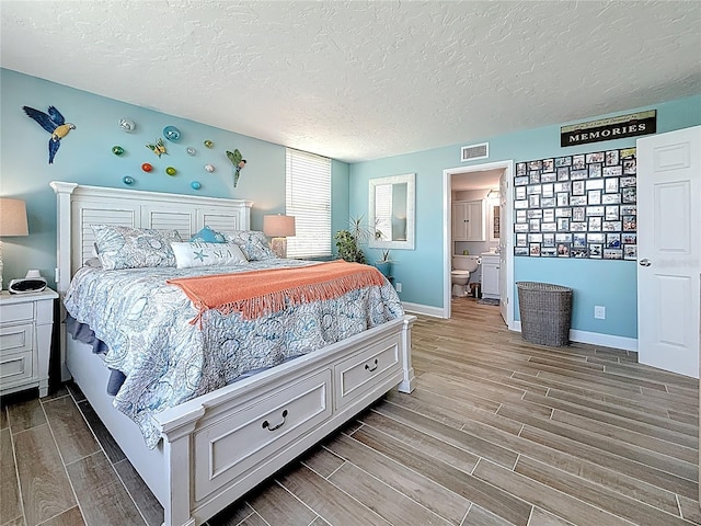 bedroom featuring wood finish floors, visible vents, baseboards, and a textured ceiling