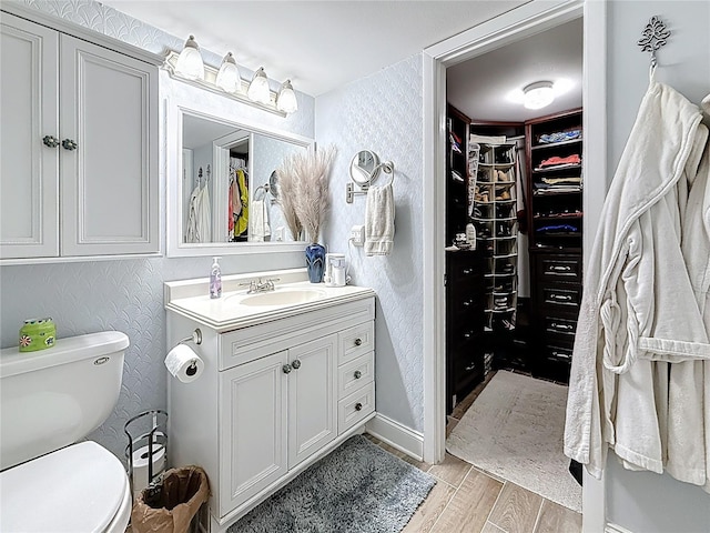 bathroom featuring a walk in closet, toilet, wood finished floors, wallpapered walls, and vanity