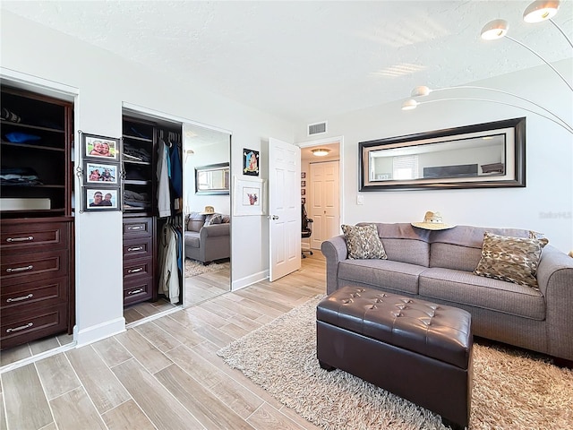 living room featuring visible vents, baseboards, a textured ceiling, and light wood-style flooring