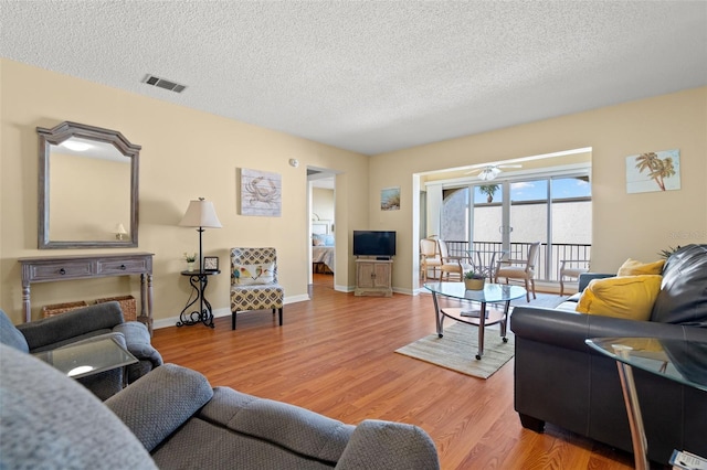 living area featuring light wood finished floors, visible vents, a textured ceiling, and baseboards