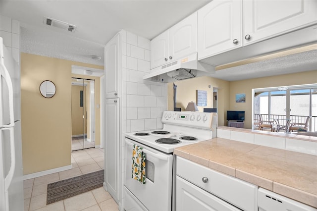 kitchen with white appliances, light tile patterned floors, visible vents, under cabinet range hood, and white cabinetry