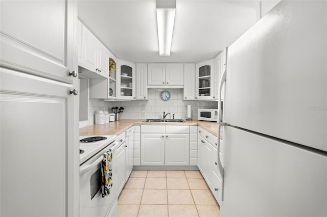 kitchen featuring a sink, tasteful backsplash, white appliances, light tile patterned flooring, and glass insert cabinets