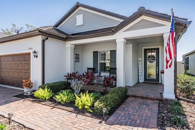 entrance to property with an attached garage, covered porch, and stucco siding