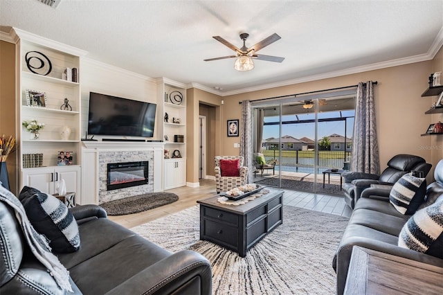 living room with light wood-style flooring, ceiling fan, a textured ceiling, a glass covered fireplace, and crown molding