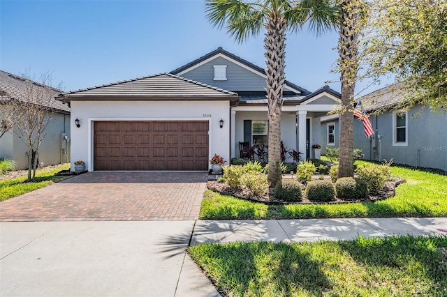 view of front of home with a tile roof, decorative driveway, an attached garage, and stucco siding