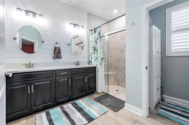 full bathroom with double vanity, wood finished floors, baseboards, and a tile shower