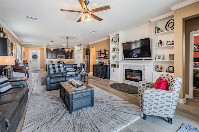 living room with visible vents, ornamental molding, light wood-style floors, and a glass covered fireplace