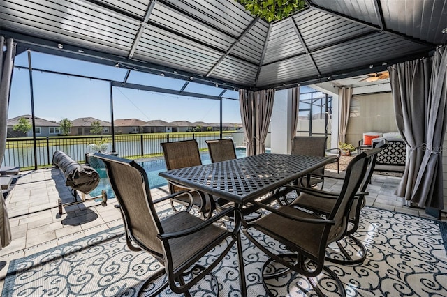 view of patio featuring outdoor dining space, glass enclosure, a water view, and a residential view