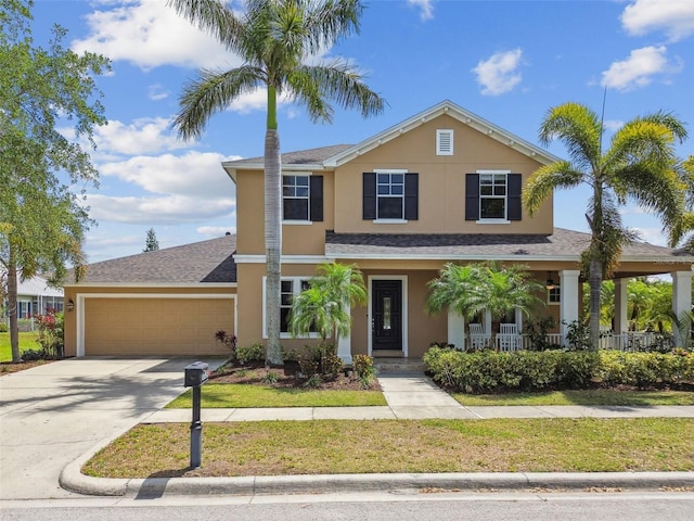 traditional home featuring a front lawn, a porch, concrete driveway, a garage, and stucco siding