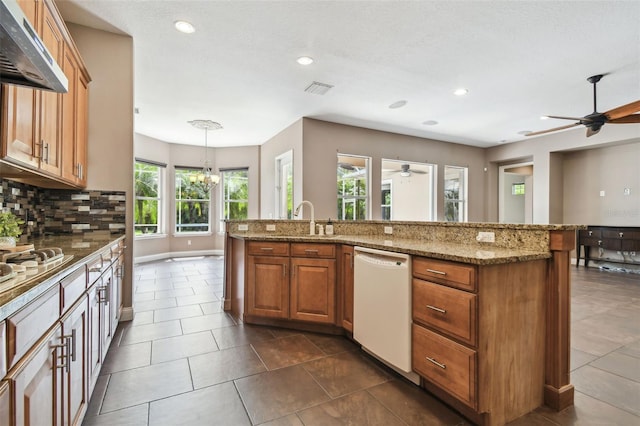 kitchen with ceiling fan with notable chandelier, decorative backsplash, brown cabinets, dishwasher, and under cabinet range hood