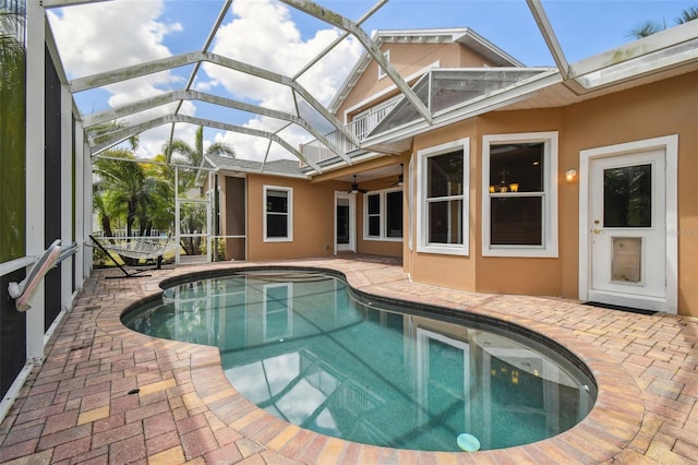 outdoor pool featuring glass enclosure, a patio, and ceiling fan