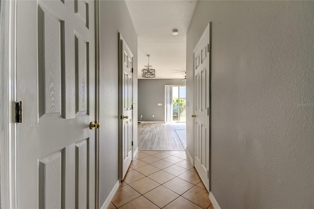 hallway featuring light tile patterned floors, a textured wall, baseboards, and a textured ceiling