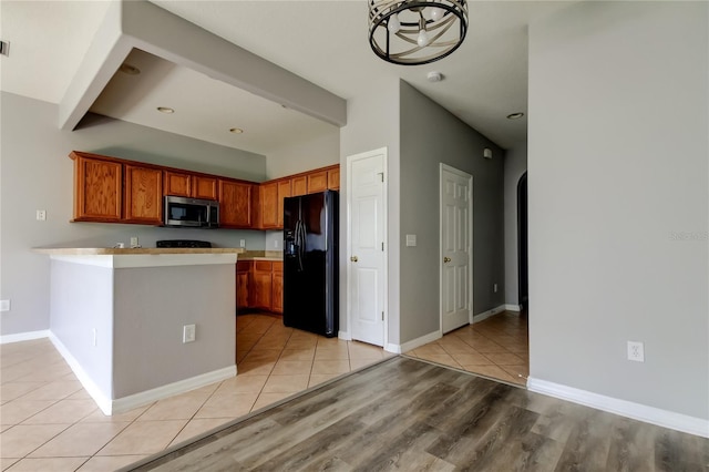 kitchen featuring stainless steel microwave, light countertops, a peninsula, arched walkways, and black fridge with ice dispenser