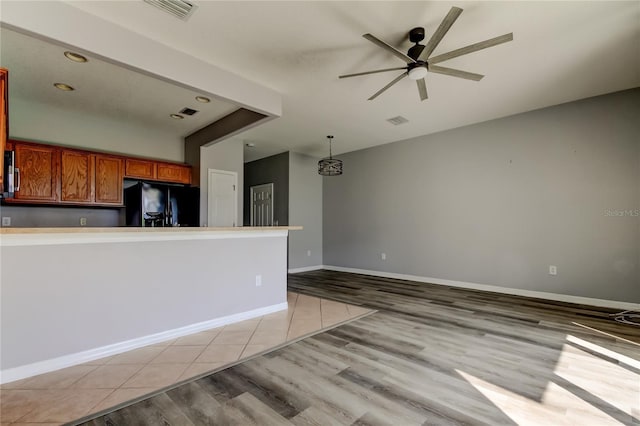 interior space with light wood finished floors, visible vents, black refrigerator with ice dispenser, brown cabinetry, and a ceiling fan