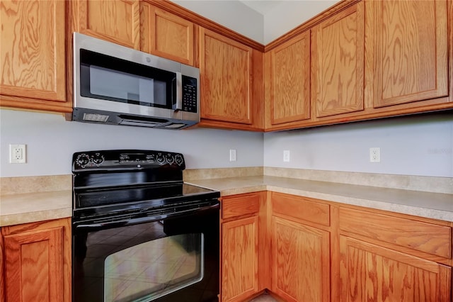 kitchen featuring stainless steel microwave, brown cabinets, light countertops, and black range with electric cooktop