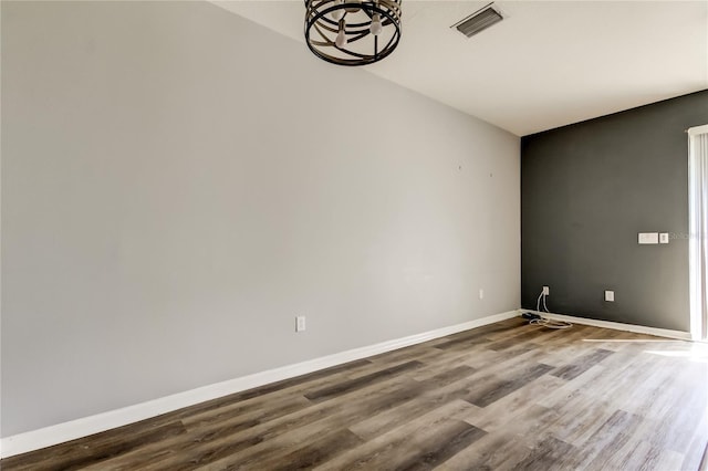 empty room with visible vents, baseboards, a notable chandelier, and wood finished floors