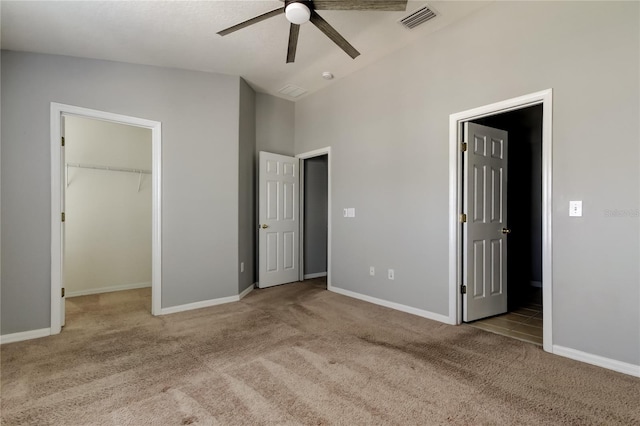 unfurnished bedroom featuring a walk in closet, visible vents, carpet floors, baseboards, and vaulted ceiling