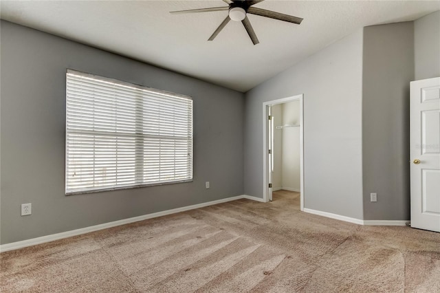 unfurnished bedroom with baseboards, carpet floors, ceiling fan, vaulted ceiling, and a spacious closet