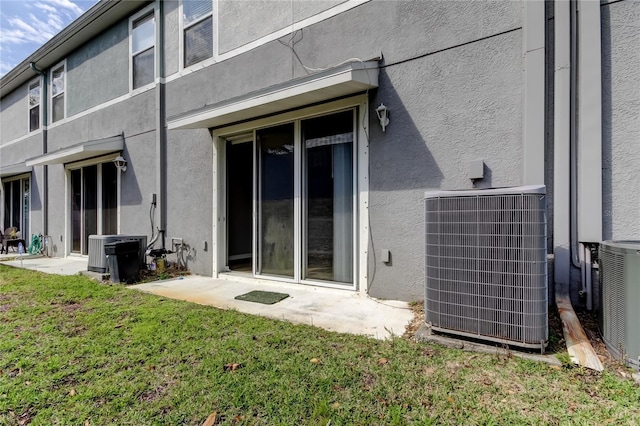 back of property with central air condition unit, a lawn, and stucco siding