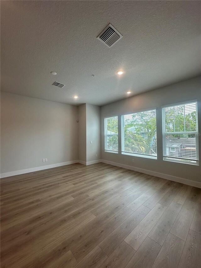 empty room with a textured ceiling, wood finished floors, visible vents, and baseboards