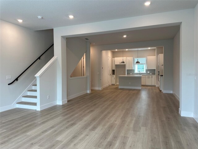 unfurnished living room featuring recessed lighting, baseboards, stairs, and light wood-style floors