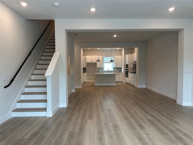 unfurnished living room with recessed lighting, stairway, baseboards, and light wood finished floors