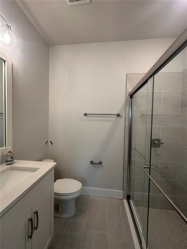 full bath featuring toilet, a stall shower, a textured ceiling, baseboards, and vanity