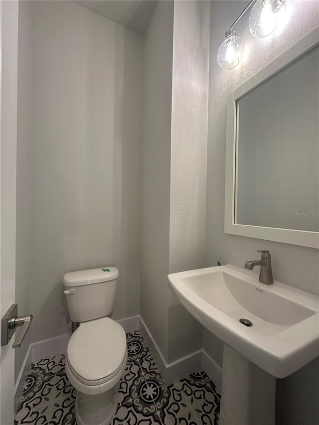 half bath with tile patterned floors, toilet, baseboards, and a sink