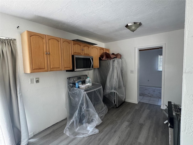 kitchen with stainless steel microwave, baseboards, brown cabinets, wood finished floors, and a textured ceiling