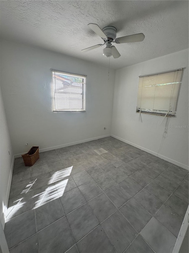 spare room with baseboards, dark tile patterned floors, a textured ceiling, and ceiling fan