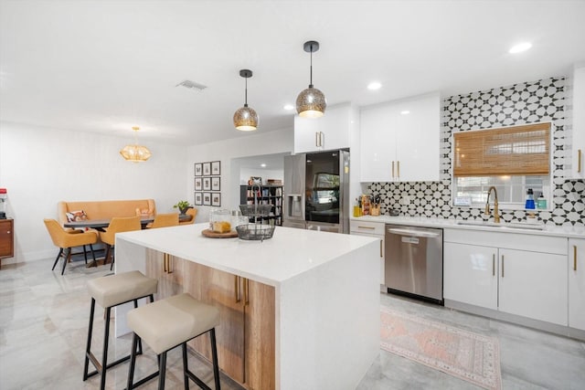 kitchen featuring visible vents, a breakfast bar area, appliances with stainless steel finishes, white cabinetry, and a sink