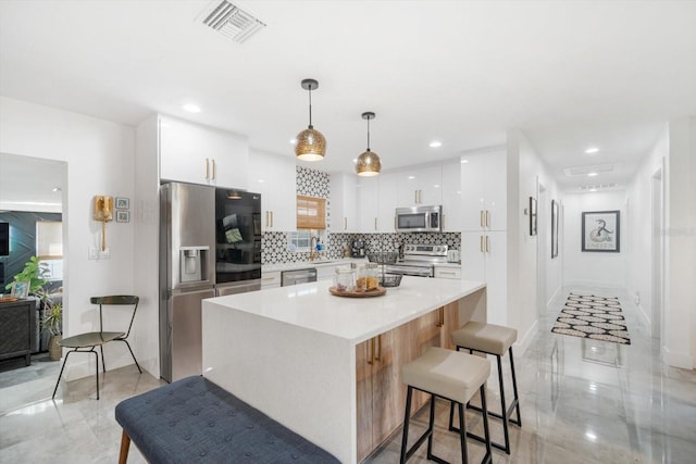 kitchen with visible vents, a kitchen bar, backsplash, white cabinetry, and appliances with stainless steel finishes