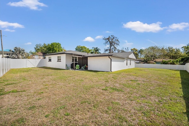 back of house with stucco siding, a lawn, and a fenced backyard