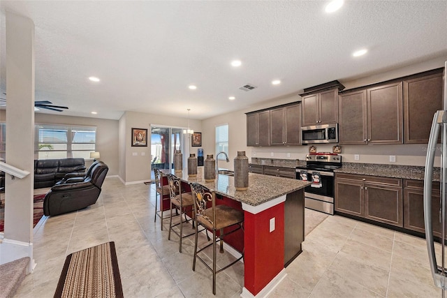 kitchen featuring a kitchen breakfast bar, open floor plan, dark stone counters, dark brown cabinetry, and appliances with stainless steel finishes