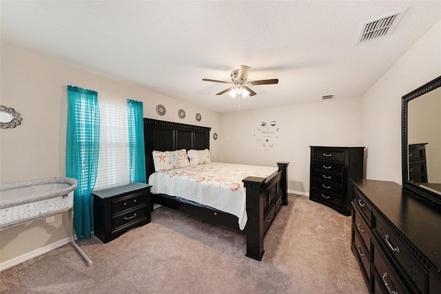 bedroom featuring a textured ceiling, light colored carpet, visible vents, and ceiling fan